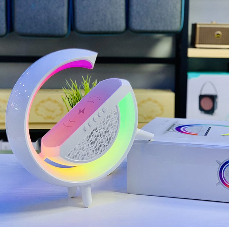 UK Technology G Lamp Wireless Charger Speaker white on a desk in the rainbow RGB mode resting on a box